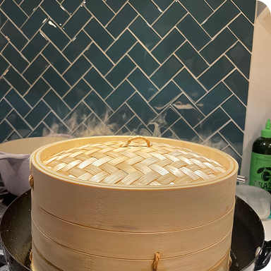 Bamboo steamer steaming pork soup dumplings on a stovetop with tiled backsplash
