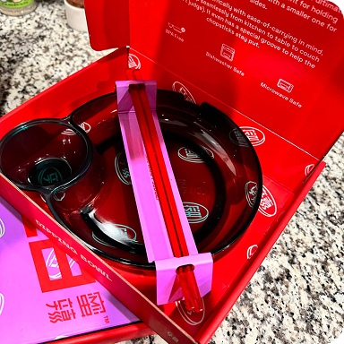 Top view of MìLà gift box with black bowl, small sauce dish, and pink silicone strap in red packaging on granite countertop